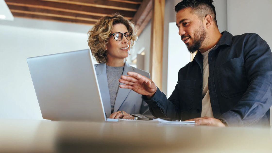 Two people discussing how recruitment process outsourcing works while looking at a laptop